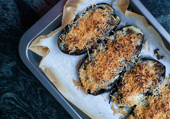 Aubergine stuffed au gratin with meat and cheese from above on a white wooden table of a rustic kitchen.