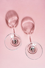 A glasses on a pastel pink background. Bright sunshine. Spectacular shadow from the glass. The...
