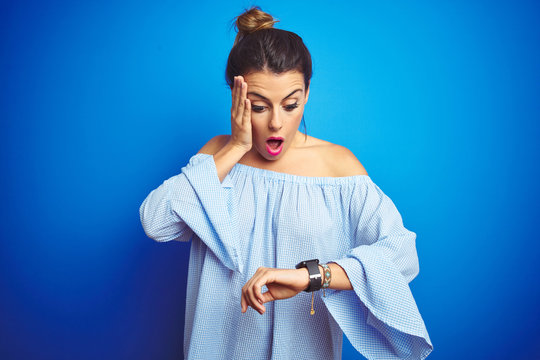Young beautiful woman wearing bun hairstyle over blue isolated background Looking at the watch time worried, afraid of getting late