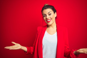 Young beautiful business woman standing over red isolated background smiling cheerful with open arms as friendly welcome, positive and confident greetings