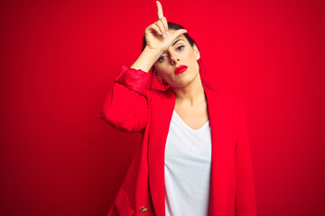 Young beautiful business woman standing over red isolated background making fun of people with...