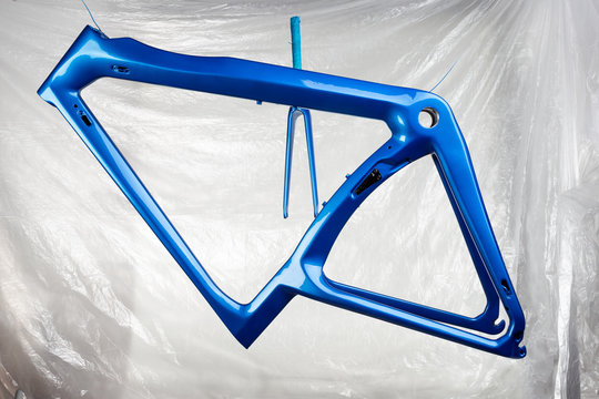 shiny new fresh fresh paintwork coating paint of a metallic blue carbon racing road bicycle frame set with fork in front of paint booth. cycling production concept background
