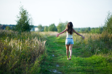 Naklejka na ściany i meble girl in denim shorts with her hair running away barefoot along a country road. copy space