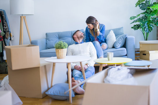 Young beautiful couple sitting on the sofa drinking cup of coffee at new home around cardboard boxes