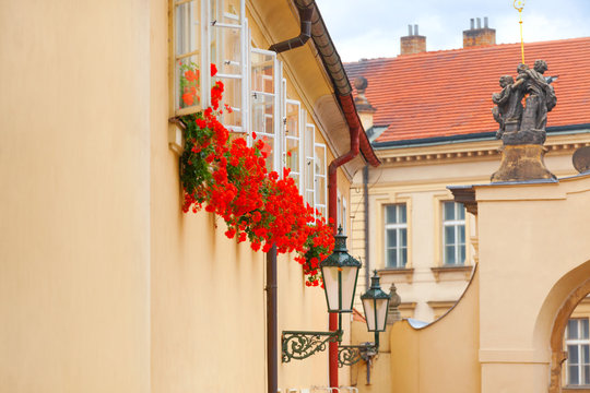 The famous lovely architecture details of Old Town Prague. Yellow walls of houses, windows with flowers, red tiled roofs, antique lanterns and statue
