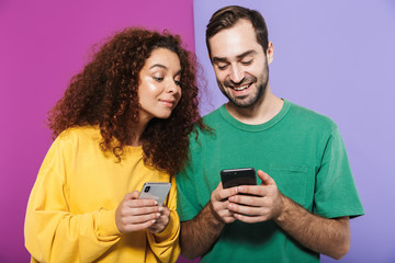 Fototapeta premium Portrait of joyful caucasian couple man and woman in colorful clothing smiling and holding cellphones together