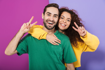 Obraz na płótnie Canvas Portrait of happy caucasian couple man and woman in colorful clothing hugging while showing peace fingers