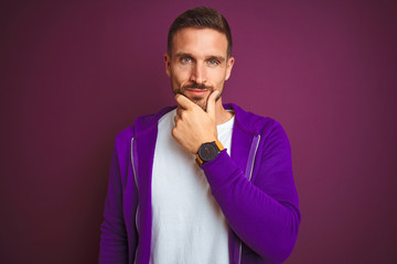 Young fitness man wearing casual sports sweatshirt over purple isolated background looking confident at the camera with smile with crossed arms and hand raised on chin. Thinking positive.