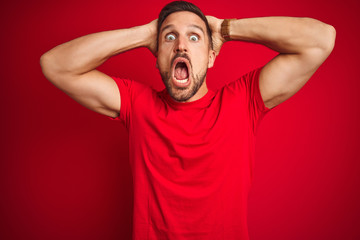 Young handsome man wearing casual t-shirt over red isolated background Crazy and scared with hands on head, afraid and surprised of shock with open mouth