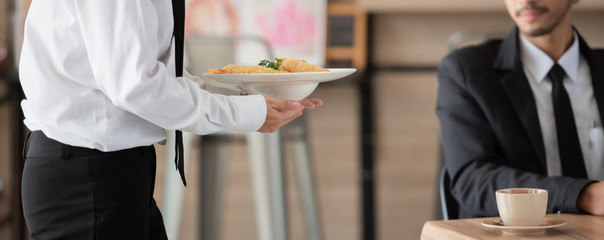 Waiter with plate of food in hand serving at table at restaurant, health care concept.