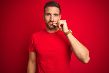 Young handsome man wearing casual t-shirt over red isolated background mouth and lips shut as zip...