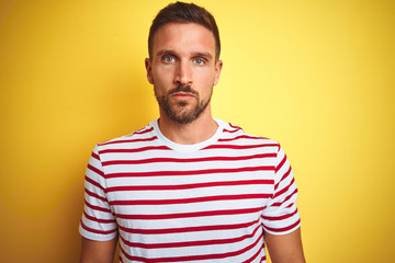 Fototapeta premium Young handsome man wearing casual red striped t-shirt over yellow isolated background Relaxed with serious expression on face. Simple and natural looking at the camera.
