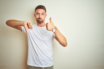 Young handsome man wearing casual white t-shirt over isolated background Doing thumbs up and down,...