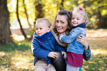Fototapeta na wymiar Beautiful young mother with small twins on a walk in autumn forest.