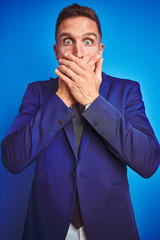 Vertical angle picture of young handsome business man over blue isolated background shocked covering mouth with hands for mistake. Secret concept.
