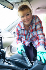 Girl is vacuuming car interior and smiling. A woman with red hair is engaged in professional cleaning of vehicles.