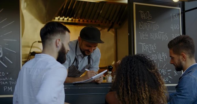 Cheerful waiter taking order from multi-racial customers at counter, Mexican street food served from a food truck. 4K UHD RAW graded footage - Powered by Adobe