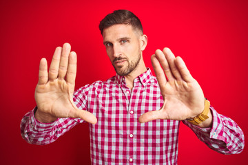 Naklejka premium Young handsome man over red isolated background doing frame using hands palms and fingers, camera perspective