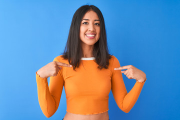Young beautiful chinese woman wearing orange t-shirt standing over isolated blue background looking...