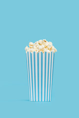 Popcorn palomitas de maíz dentro de una caja de cartón a rayas blancas y celeste sobre fondo un celeste liso y aislado. Vista de frente y de cerca. Copy space. Formato vertical