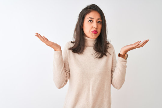 Beautiful chinese woman wearing turtleneck sweater standing over isolated white background clueless and confused expression with arms and hands raised. Doubt concept.