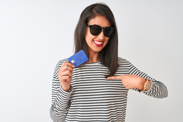 Young chinese woman wearing sunglasses holding credit card over isolated white background with surprise face pointing finger to himself