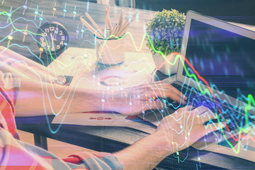 Double exposure of stock graph with businessman typing on computer in office on background. Concept of hard work.