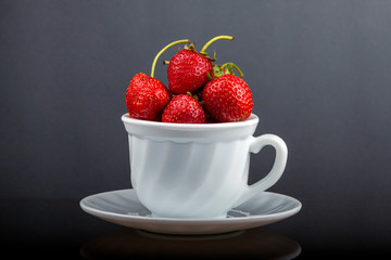 On a black glass table is a cup with strawberries