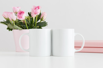 Two mugs mockup with books and pink roses in a pot on a white table.