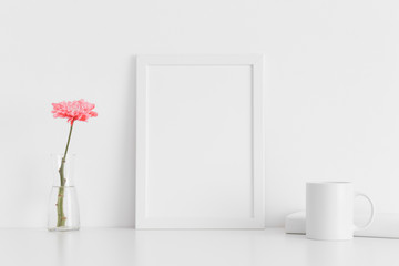 White frame mockup with a chrysanthemum in a vase, book and a mug on a white table. Portrait orientation.
