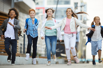 Fototapeta premium Group of happy children in casual clothing smiling and running together in the city outdoors