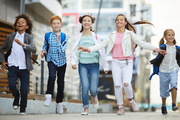 Group of happy children in casual clothing smiling and running together in the city outdoors