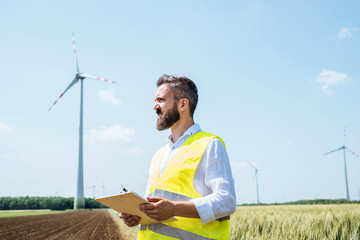 An engineer standing on a field on wind farm, making notes.