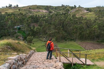 Fototapeta na wymiar Young male tourist traveling alone in Sacred valley. Solo man hiker with backpack sightseeing inca ruins in Cusco region, Peru
