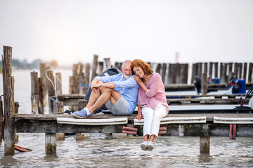 Senior couple on a holiday sitting by the lake, hugging.