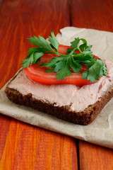 A slice of black rye bread with chicken paste, tomato and parsley. Delicious sandwiches for a snack on the table.  Cold appetizer on a red wooden board. 