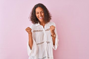 Young brazilian woman wearing shirt standing over isolated pink background excited for success with arms raised celebrating victory smiling. Winner concept.