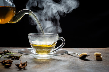 Process brewing tea,Cup of freshly brewed fruit and herbal tea, dark mood.The steam hot water is...