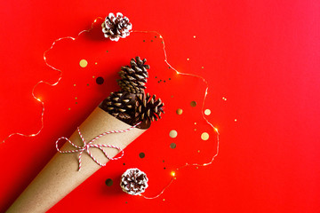 Pine cones in paper cone with lights, winter holiday christmas vivid red background with copy space.