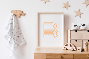 Fototapeta na wymiar Stylish scandi childroom withwooden mock up photo frame, wooden toys, boxes, blocks and accessories Stars pattern on the background wall. Bright and sunny interior with wooden desk. Home decor.