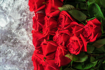 Bright red roses with green leaves lie on a dark background.
