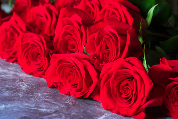 Bright red roses with green leaves lie on a dark background.