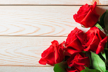 Bright red roses with green leaves lie on a light natural wooden background with place for text.