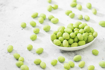 Peanuts in wasabi in a white plate on a light table