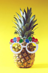 Pineapple with happy birthday glasses on yellow background. Minimal concept, retro style.