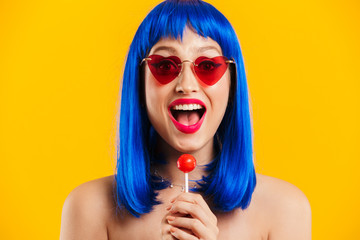 Portrait of glamorous astonished woman wearing blue wig and sunglasses holding lollipop