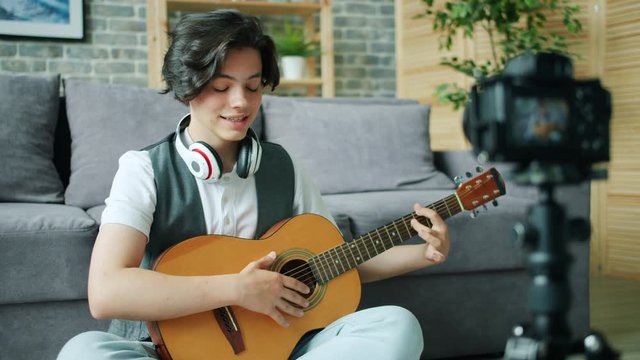 Teenage musician young boy is recording video holding guitar using modern camera in apartment. Musical instruments, childhood and occupation concept.