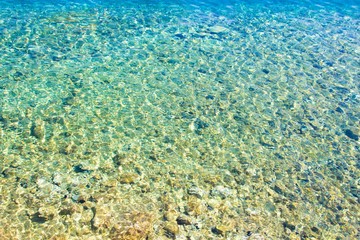 Clear amazing azure coloured sea water. Transparent sea water with sunlight on pebbles. Sea water background.