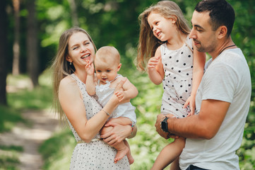 Mom, dad and two little daughters having fun in the summer park.