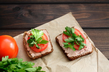 A slice of black rye bread with chicken paste, tomato and parsley. Cold appetizer on a brown wooden table. Delicious sandwiches for a snack on the table.